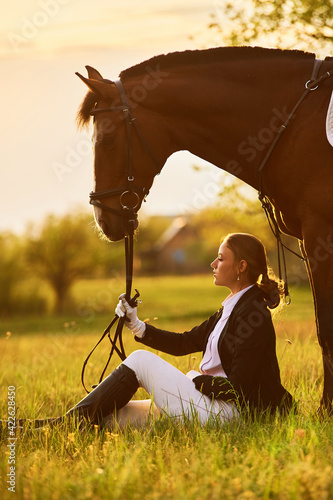 horse rider girl sitting in a meadow near her horse  
