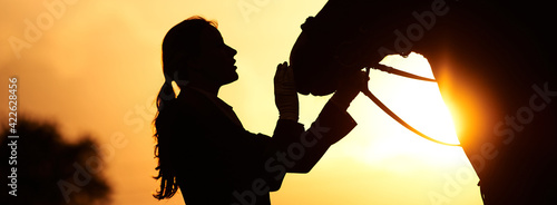 A horse rider girl stroking the head of a horse in the rays of the setting sun. Silhouette of a girl and a horse 