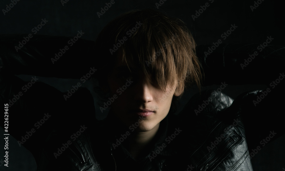 Portrait image of a young guy with long hair on a very dark background Portrait image of a young guy with long hair on a very dark background