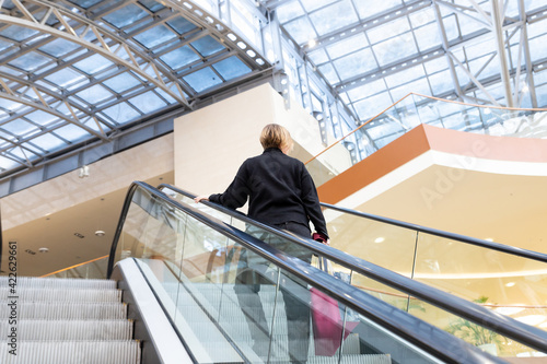woman on escalator staircase in business centre.Rear view of woman while using escalator in shopping mall for moving to another floor. Cocneptual of woman when visit shopping mall.