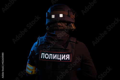 Male in black uniform conforms to Police SWAT. Patch on the back with the inscription Police in Russian. Black background (red and blue lights) photo