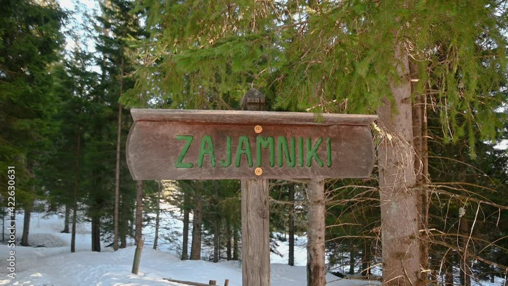 Wooden sign of Alpine village Zajamniki in pristine forest in Slovenia. Snow covering forest floor in winter. Handheld Wooden sign of Alpine village Zajamniki in pristine forest in Slovenia. Snow covering forest floor in winter. Handheld