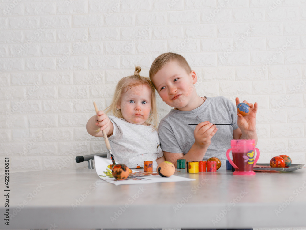 two children paint eggs in the kitchen on the eve of the Easter holiday two children paint eggs in the kitchen on the eve of the Easter holiday