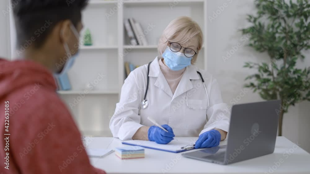 Doctor and patient talking in protective face masks, pandemic precautions Doctor and patient talking in protective face masks, pandemic precautions