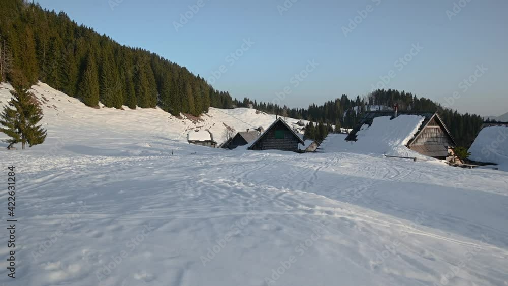 Idyllic Alpine village in mountains, Slovenia. Snow covering landscape in winter. Wooden traditional cottages. Herdsmen settlement with many huts and cabins in the Alps. Right pan, wide angle