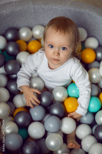 girl child sits in a pool with colorful plastic balls