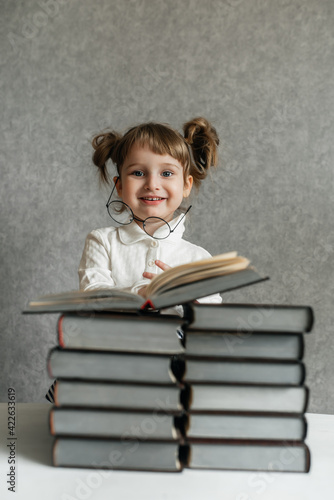 Happy funny baby girl in glasses reading a book. Emotional girl. To school soon