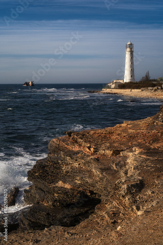 Lone beacon guards the ships. The lighthouse shows the way for boats. Wrecked ship lays nearby