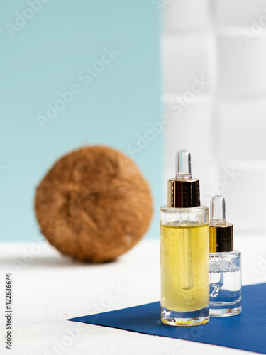 Coconut oil skin care serum with coconut on blue background. Skin beauty and health concept.
