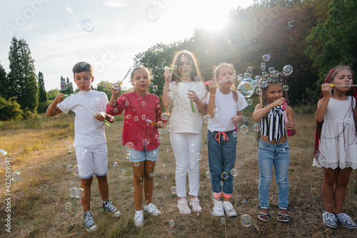 A large group of cheerful children play in the Park and inflate soap bubbles. Games in a children's camp