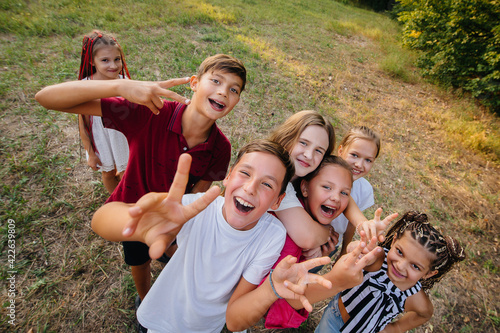 A large group of cheerful children sit on the grass in the Park and smile. Games in a children's camp