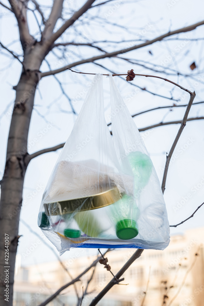 cellophane bag with plastic bottles and tin on tree, ecology concept