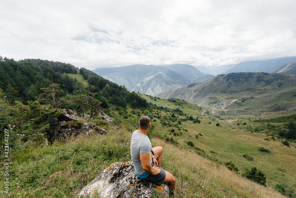 A young man sits and enjoys a stunning view of the beautiful mountains while traveling. Wildlife A young man sits and enjoys a stunning view of the beautiful mountains while traveling. Wildlife