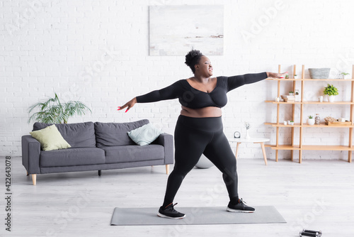 full length of pleased african american overweight woman in sportswear exercising at home