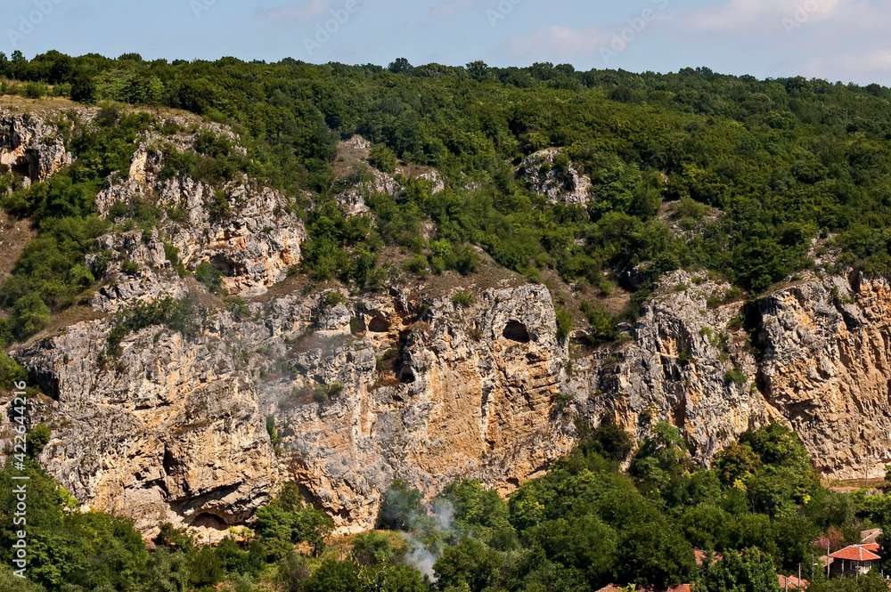 View of the beautiful village of Nisovo, Bulgaria, located below, above and in the high limestone cliffs, protected by magnificent deciduous trees View of the beautiful village of Nisovo, Bulgaria, located below, above and in the high limestone cliffs, protected by magnificent deciduous trees