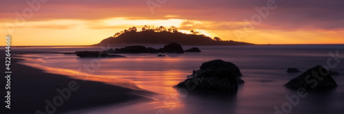 Panorama long exposure of an orange sunrise across a seascape scene of rocks looking out towards the silhouette of Green Island at Cunjurong Point, New South Wales Australia