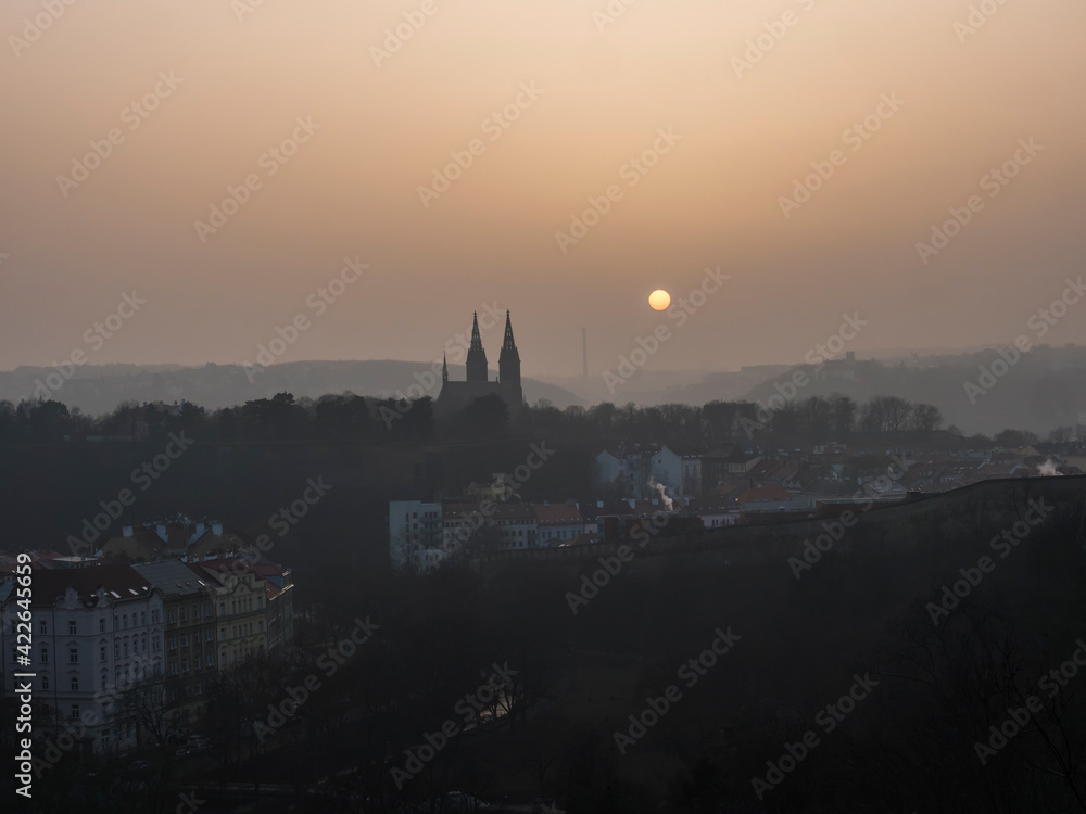 Aerial view over Prague 2 district from Nusle bridge, nuselsky most with typical architecture, old defense wall of Vysehrad castle and Basilica of St. Peter and Paul towers with orange sun in haze