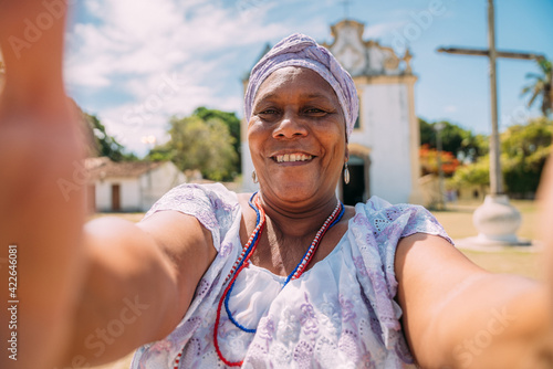 Happy Brazilian woman of African descent dressed in the traditional Bahian dress making a selfie in front of the church. focus on face photo