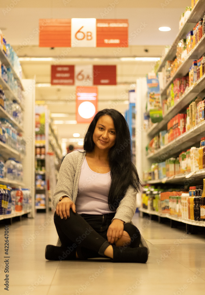 Happy young girl smiling with a lead jacket and black pants sitting in the aisle of a store
