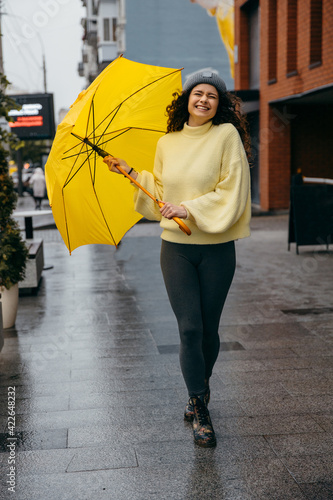 Charming young curly woman use yellow umbrella at the street of megapolis city in rainy day