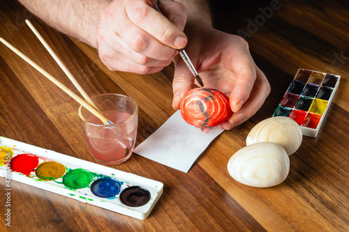 Man hands make brush strokes with watercolors on wooden eggs. Traditional and festive entertainment before Easter