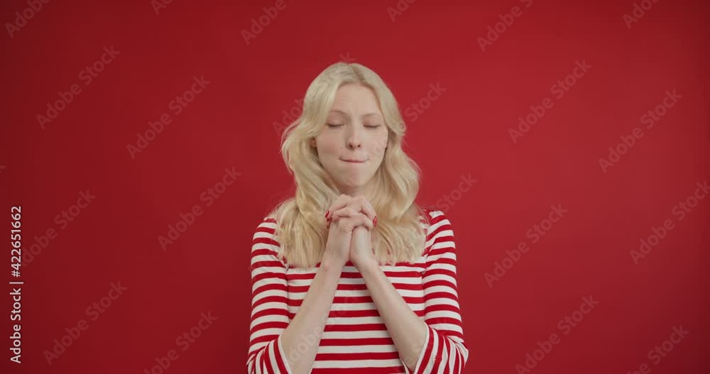 Charming young woman clasping hands with hopeful expression, dreaming and fantasizing, visualizing pleasant memories. Indoor studio shot isolated on red background Charming young woman clasping hands with hopeful expression, dreaming and fantasizing, visualizing pleasant memories. Indoor studio shot isolated on red background