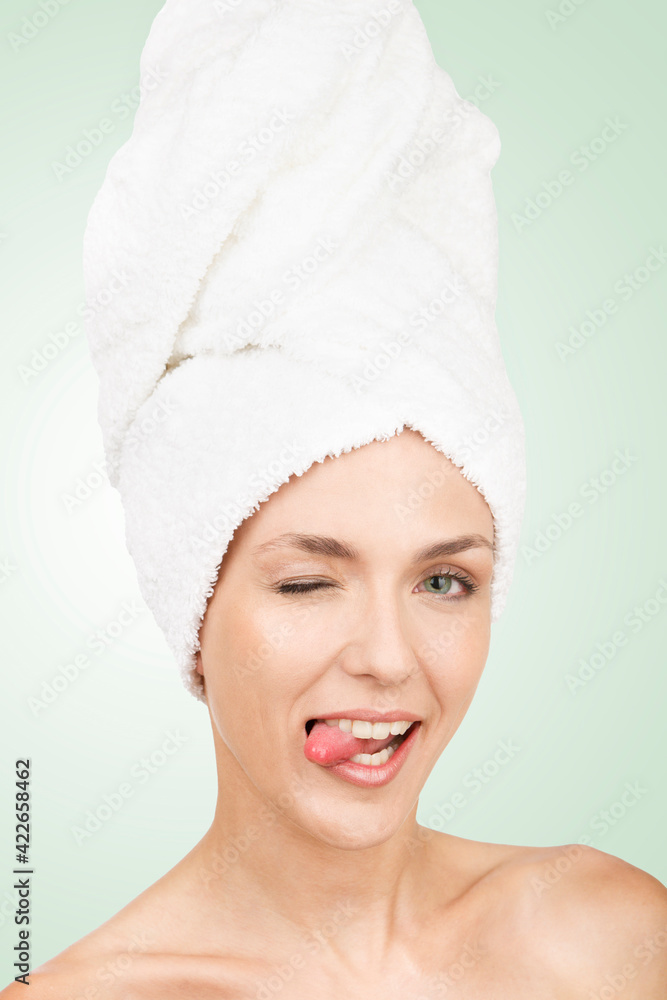 young girl with towel on head gesturing. Sticking out his tongue in a mocking and mischievous attitude. Green background. Aesthetic concept young girl with towel on head gesturing. Sticking out his tongue in a mocking and mischievous attitude. Green background. Aesthetic concept