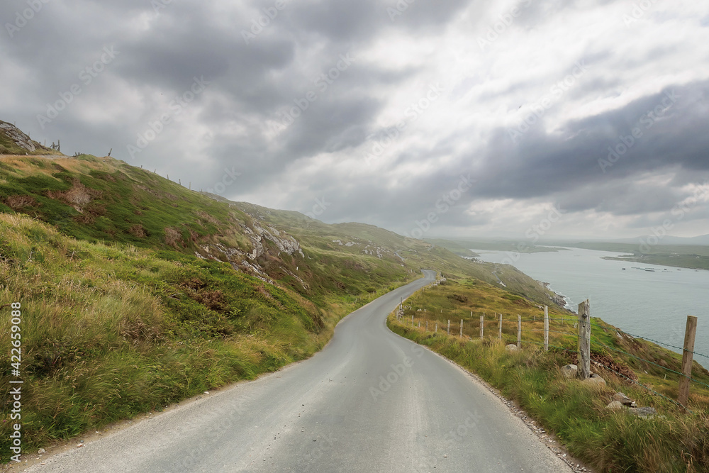 Small narrow asphalt road with beautiful unique views, Sky road loop near Clifden town, county Galway, Ireland. Cloudy sky. Irish scenery. Nature landscape. Popular tourist travel destination