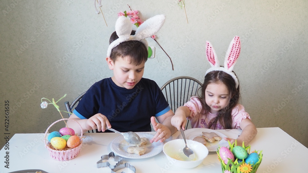boy and girl are preparing cookies for easter, laughing. Having fun on Easter egg hunt. Child boy and girl wearing bunny ears and painting eggs. colorful eggs boy and girl are preparing cookies for easter, laughing. Having fun on Easter egg hunt. Child boy and girl wearing bunny ears and painting eggs. colorful eggs