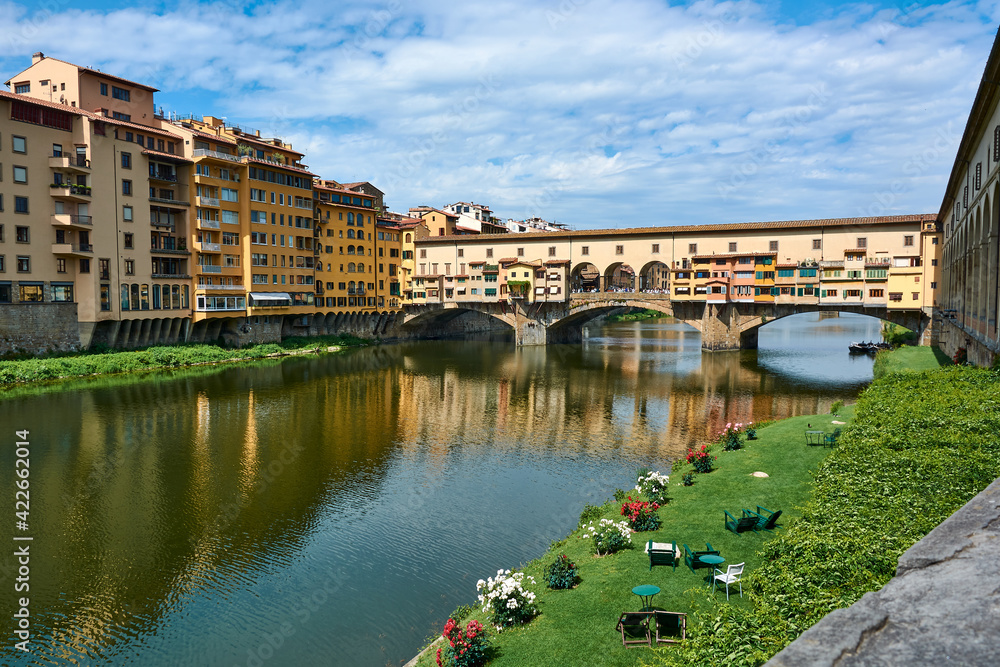 An horizontal view of Ponte Vecchio and picturesque buildings on a beautiful sunny spring day with blue sky in Florence, Italy. Popular medieval bridge spanning the Arno river.