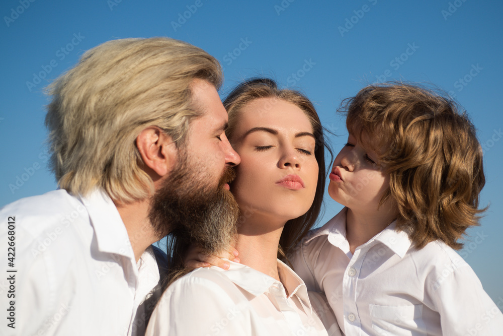 Fototapeta premium Happy family outdoors. Father and son embrace and kissing mother. Young smiling family with child having fun together. Kids love and hug mom. Smile face. Mothers day. Parents and children.