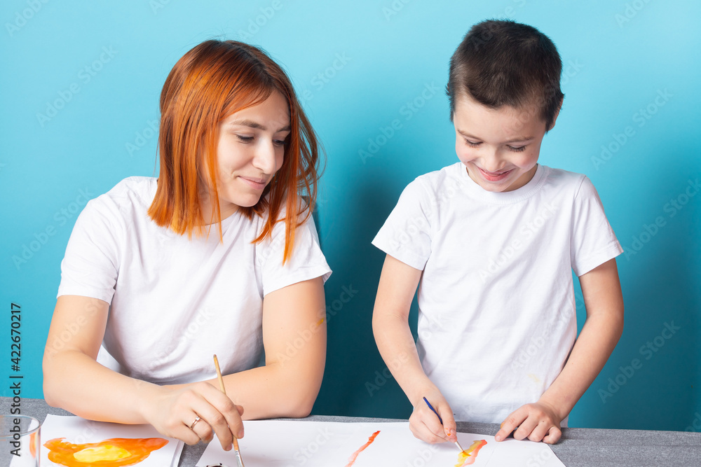 Children's creativity. Mother and son paint with paint on blue background Children's creativity. Mother and son paint with paint on blue background
