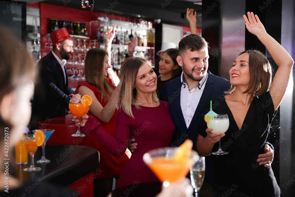 Young man and two women with cocktails having fun at nightclub