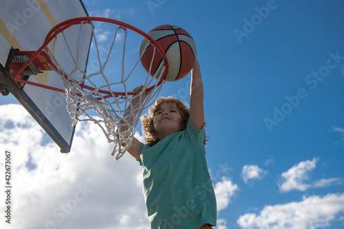 Active kids enjoying outdoor game with basketball. Basketball child player running up and dunking the ball.