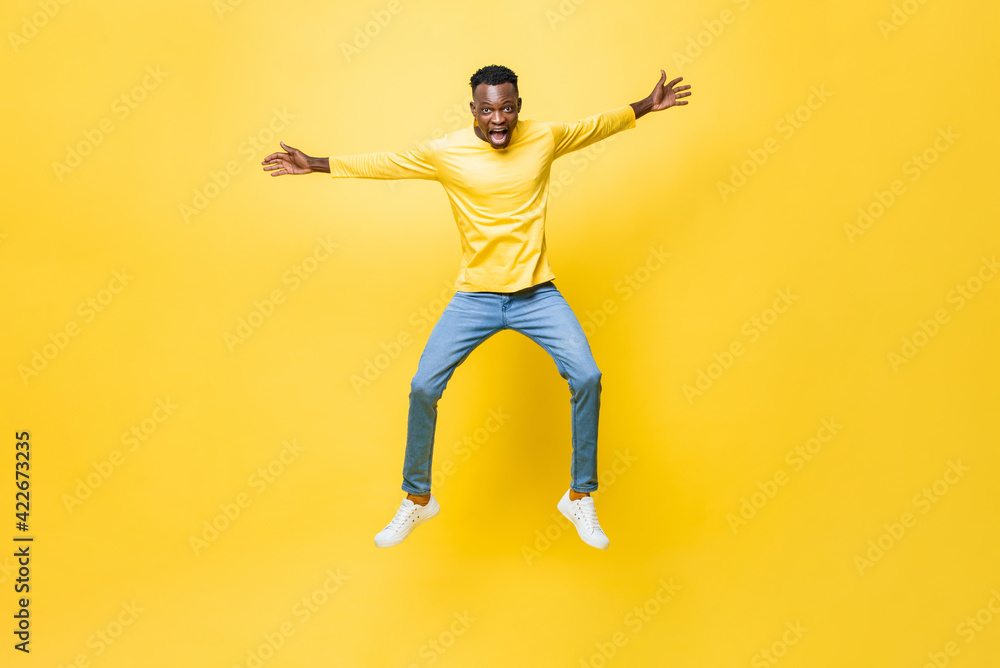 Young excited African man jumping with outstretched hands isolated on yellow studio background