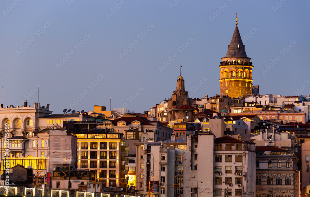 Picturesque view of lighted Galata Tower topping over residential buildings of Beyoglu district in Istanbul in winter evening.