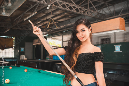 A beautiful and young asian billiard player at an open air and old pool hall. Third world and exotic ambiance.