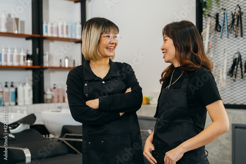 Canvas Print Happy young Asian female hairstylist colleagues working in salon standing wearin