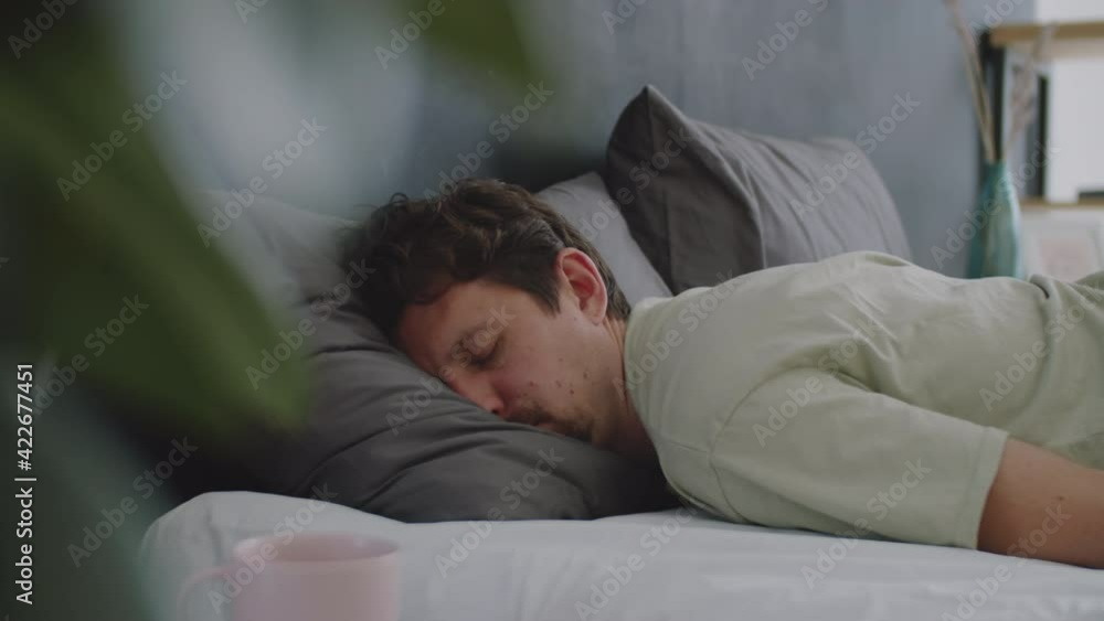 Tracking shot of tired Caucasian man falling down on stomach on bed with eyes closed and sleeping