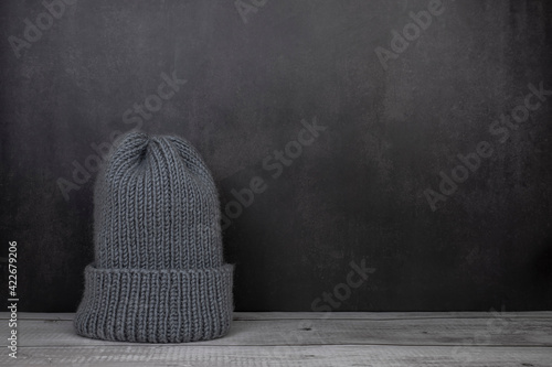 one gray knitted hat stands on the table and with a gray background, hat for sale