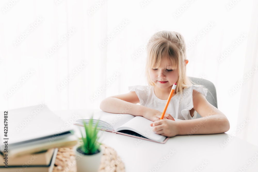 Girl writes in notebook at table. Education concept. Home schooling. Homework. Girl writes in notebook at table. Education concept. Home schooling. Homework.