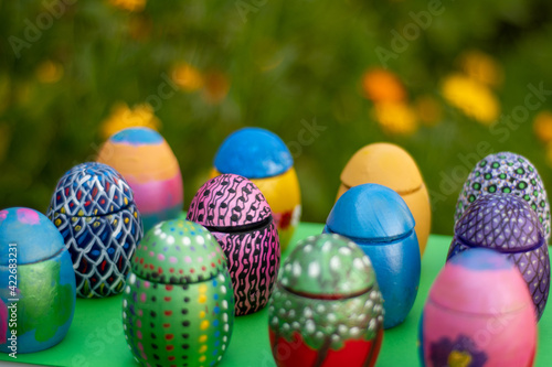 Hand-made Easter eggs on a green pedastal in front of yellow and orange spring flowers photo