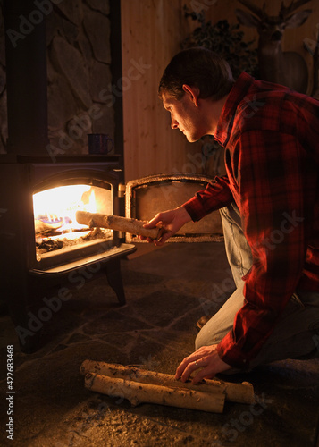 rustic adult man loading wood into woodburning stove at night
