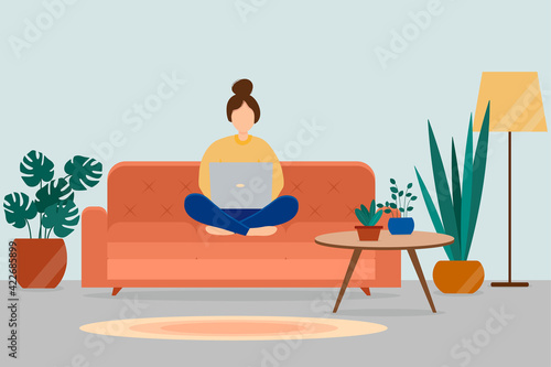 A girl with a laptop sits on a sofa in a cozy living room. Work at home and freelance concept.