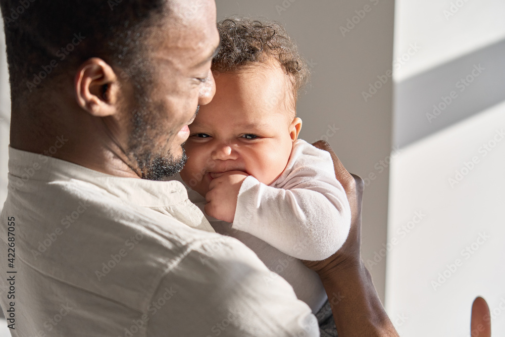Fototapeta premium Happy tender African American man father holding cute adorable little child daughter enjoying sweet moment of love. Smiling affectionate Black dad hugging infant kid baby feels proud about fatherhood