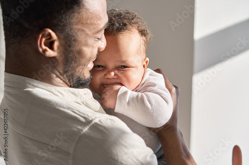 Happy tender African American man father holding cute adorable little child daughter enjoying sweet moment of love. Smiling affectionate Black dad hugging infant kid baby feels proud about fatherhood © insta_photos