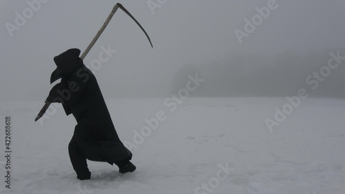Plaque doctor in black bird beak mask with scythe goes through a snowy field in mist.   Image of all pandemics