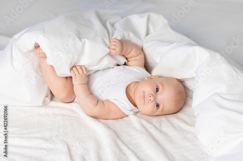 happy baby on the bed in the morning. Textiles and bed linen for children. A newborn baby has woken up or is going to bed