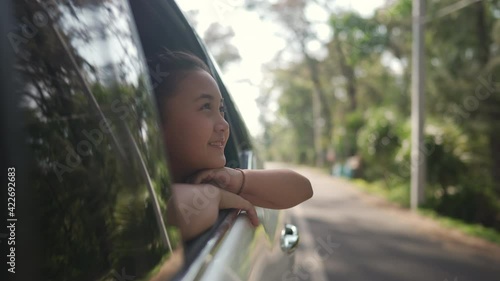 Happy Asian family enjoy and having fun together with outdoor lifestyle activity on road trip vacation. Little child girl kid sit in the car with pull her face and hand out of car window in summer day