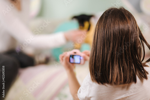 Young daughter photographer make photo of her mom play with dog at home. Toy camera for kids